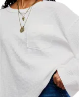Camiseta blanca de punto waffle en algodón, con silueta relajada, hombros caídos, mangas largas, bolsillo frontal y escote amplio tipo barco.
