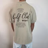 Chomba color beige con cuello clásico, corte oversize, mangas cortas y bordados marrones con la inscripción "Golf Club" y otros motivos. 