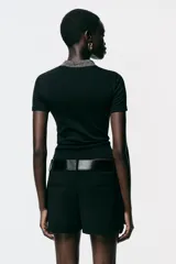 Chomba negra de corte slim fit, con cuello polo y mangas cortas. Presenta un falso bolsillo en el pecho y cierre frontal con botones. Detalle de hilo metalizado en cuello, bolsillo y tapeta.