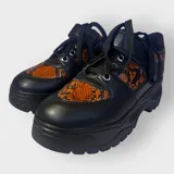 Zapatillas negras con detalles en animal print naranja y cordones negros.