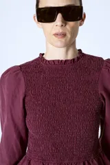 Blusa color borgoña con escote redondo con volados, mangas largas abullonadas y cuerpo fruncido.