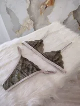 Conjunto de lencería de encaje verde musgo con detalles en beige, compuesto por un corpiño triangular sin aro y una tanga con tiras ajustables.