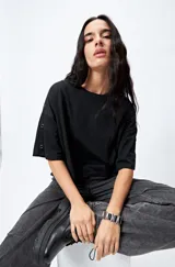 Remera cropped negra de mangas cortas amplias con ojales metálicos a lo largo de las mangas.