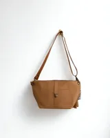 Riñonera bandolera de cuero color marrón claro, con correa regulable y bolsillo frontal con broche metálico. Presenta una pequeña raya de lapicera en el frente. Producto en SALE, sin cambio.