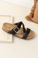 Sandalias bajas color marrón, con base de corcho y tiras de cuero cruzadas con hebilla metálica ajustable.