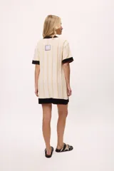 Vestido de tejido de punto color amarillo con rayas verticales en tono más claro. Presenta cuello redondo y puños en color celeste con terminación de pespunte en color naranja. Lleva un bordado de iniciales en el pecho.