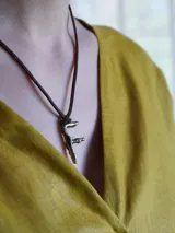 Gargantilla marrón de cuero con dije de bronce en forma de letra M.