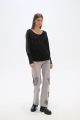 Sweater negro de tejido acanalado, corte holgado tipo murciélago con mangas largas ajustadas en puños. Escote bote adornado con apliques de pedrería plateada que se extienden por los hombros y mangas.