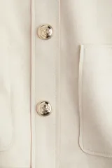 Saco corto color beige de tejido de punto con acabado cepillado suave, cuello redondo, cierre frontal con botones metálicos dorados y bolsillos de parche delanteros.