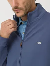 Buzo azul con cuello alto, cierre frontal y logo bordado en el pecho.