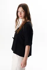 Chaqueta color beige con escote en V y cierre frontal con lazos. Presenta mangas cortas con volados.