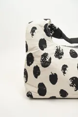 Bolso tipo tote bag con estampado de lunares irregulares en blanco y negro, con base y asas cortas en color negro.