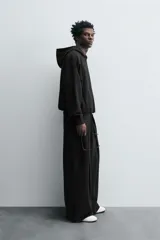 Pantalón jogger negro de corte relaxed fit, confeccionado en tejido de algodón. Presenta cintura elástica ajustable con cordón, pliegues frontales, bolsillos delanteros y un bolsillo trasero.