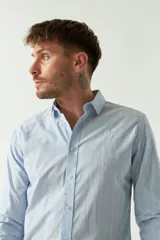 Camisa de hombre a rayas verticales celestes y blancas, corte slim fit, manga larga, logo bordado en el pecho y cartera con botones.