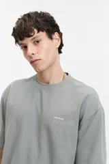 Remera de manga corta color verde grisáceo, corte oversize con cuello redondo y estampado con la frase 'STRAL STYLE ONL' en la espalda.