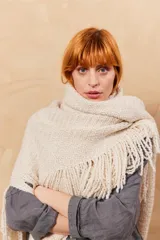 Chal triangular de tejido de punto color crudo con flecos en el borde inferior.