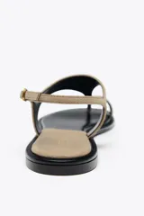 Sandalia plana color beige de cuero gamuzado, con tira entre los dedos y pulsera con hebilla ajustable.