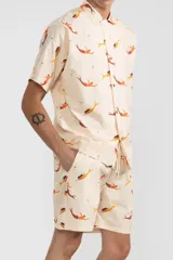 Short de tela color crema con estampado de sirenas en tonos naranja y amarillo. Tiene cintura elástica con cordón ajustable, bolsillos laterales y un bolsillo trasero.