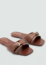 Sandalias planas color marrón cuero, con punta cuadrada, diseño de tiras y hebilla decorativa.