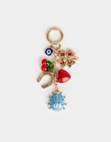 Llavero metálico dorado con dije de mosquetón y charms colgantes: ojo turco, trébol de cuatro hojas con la palabra "LUCK", cerezas, herradura, corazón rojo y mariquita celeste con lunares negros.