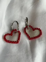Par de aros colgantes con forma de corazón, con borde de strass rojos y aro superior plateado.