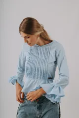 Camisa blanca de mangas largas con volados en los puños, con pechera plisada y chaleco color crema con botones.