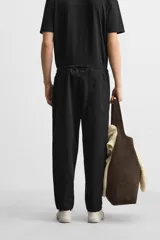 Pantalón de hombre color beige, corte carrot fit, con cintura elástica ajustable con cordón, bolsillos frontales y bolsillo trasero de plastrón.