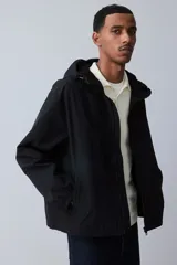 Campera rompevientos negra de nylon repelente al agua con protección UV, corte regular, cierre frontal, capucha con cordón de ajuste elástico, puños elásticos, bolsillos laterales y bolsillo interior con cierre, forro de malla y cordón de ajuste elástico oculto en el bajo.