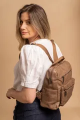 Mochila mediana de símil cuero color beige, con asa superior, dos compartimentos principales con cierre y dos bolsillos frontales con cierre. Las correas son ajustables y de color beige.