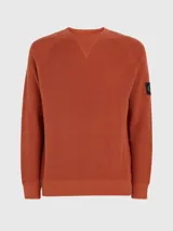 Sweater de punto texturizado color ladrillo, con cuello redondo, mangas largas raglán y logo de Calvin Klein en la manga.