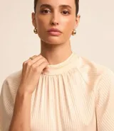 Blusa de mangas cortas confeccionada en chiffon color crema, con cuello alto, cavas raglán, cierre por gota y textura rayada.
