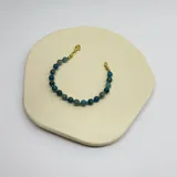 Pulsera elástica con cuentas de apatita azul verdoso de 6mm, separadores de hilo turquesa y terminaciones de acero hipoalergénico con baño dorado.