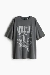 Remera de manga corta, corte oversized y lavado oscuro (gris/negro), con estampado frontal que incluye el texto "NIRVANA" y una imagen de una flor.