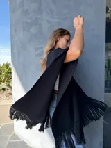 Ruana negra de lana con flecos en los bordes y detalles en cuero color cobre.