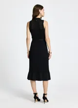 Vestido midi tejido negro con cuello alto, sin mangas, calado y falda con volantes. Incluye cinturón con hebilla irregular.