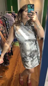 Vestido corto color verde lima con estampado floral blanco, corte cheongsam, cuello mao, sin mangas, con ribete negro y lazos decorativos en el lateral.