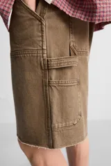 Bermuda color verde militar, de corte relaxed fit, con bolsillos frontales y traseros tipo plaqué, detalle de tira y bolsillo multifunción en la pierna, y bajo irregular.