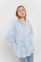 Camisa celeste de algodón con bordado calado tipo broderie, manga larga con puño angosto y botones al frente.