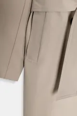 Gabardina larga color beige, con cuello solapa, manga larga con trabillas en hombros y cierre frontal cruzado con botones negros. Incluye cinturón a tono anudado.