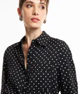 Vestido midi tipo chemise de tela satinada negra con lunares blancos, cuello solapa, abotonado delantero, mangas largas y cinturón con hebilla.