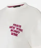 Remera blanca de algodón con corte boxy, cuello redondo y mangas cortas con dobladillo. Presenta un bordado en el pecho con la frase "PEACE NEW YORK MONEY WINE" en color borgoña.