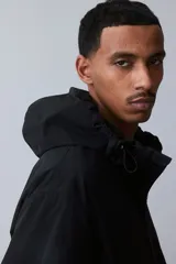 Campera rompevientos negra de nylon repelente al agua con protección UV, corte regular, cierre frontal, capucha con cordón de ajuste elástico, puños elásticos, bolsillos laterales y bolsillo interior con cierre, forro de malla y cordón de ajuste elástico oculto en el bajo.
