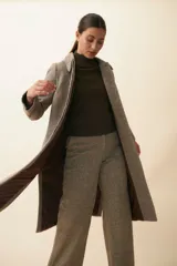 Tapado largo con cuello solapa y corte recto, color gris claro. Tiene cierre frontal con botones ocultos, tajos laterales y bolsillos escondidos en el corte lateral. Está forrado y confeccionado en lana fina sin teñir, diseñada exclusivamente por Don Baez. Hecho 100% en Uruguay.