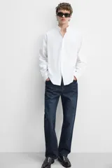 Camisa blanca de corte regular fit confeccionada en popelín de algodón. Tiene cuello abotonado, manga larga con puños abotonados y cierre frontal con botones.