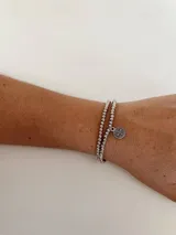 Set de dos pulseras plateadas elásticas con cuentas redondas y dije circular con una cruz calada.