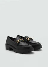 Mocasines negros de cuero sintético con hebilla dorada y suela track.
