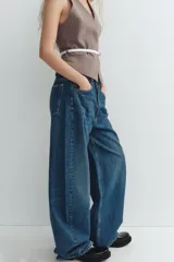 Jeans de tiro medio color azul denim, corte baggy, con trabillas y cinco bolsillos. Cierre frontal asimétrico con cremallera y botones metálicos.