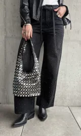 Pantalón de jean negro de corte recto, con tachas plateadas y cinturón fino con hebilla metálica.