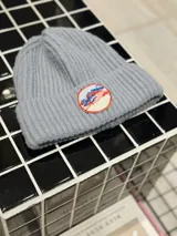 Gorro de lana celeste con diseño de punto acanalado y parche circular bordado con motivo de montañas y cielo.