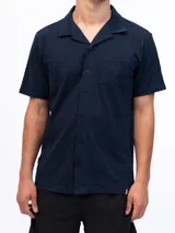 Camisa de manga corta color azul marino, confeccionada en tejido piqué de algodón. Presenta cuello cubano y cierre frontal de botones. Incluye un bolsillo de parche en el pecho izquierdo.